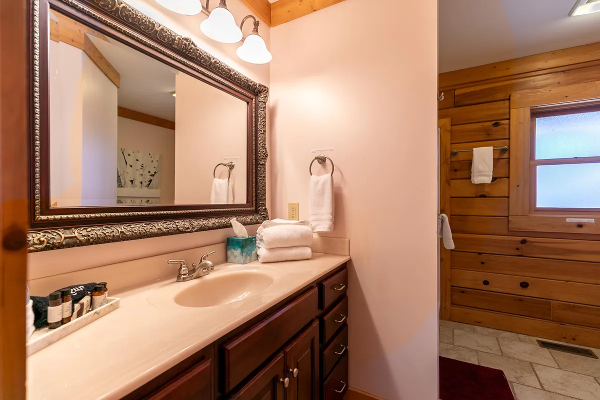 A bathroom featuring a large ornate mirror, a spacious vanity with sink, wooden cabinets, and neatly arranged towels. The overall mood is calming and spa-like, ideal for self-care rituals and relaxation.