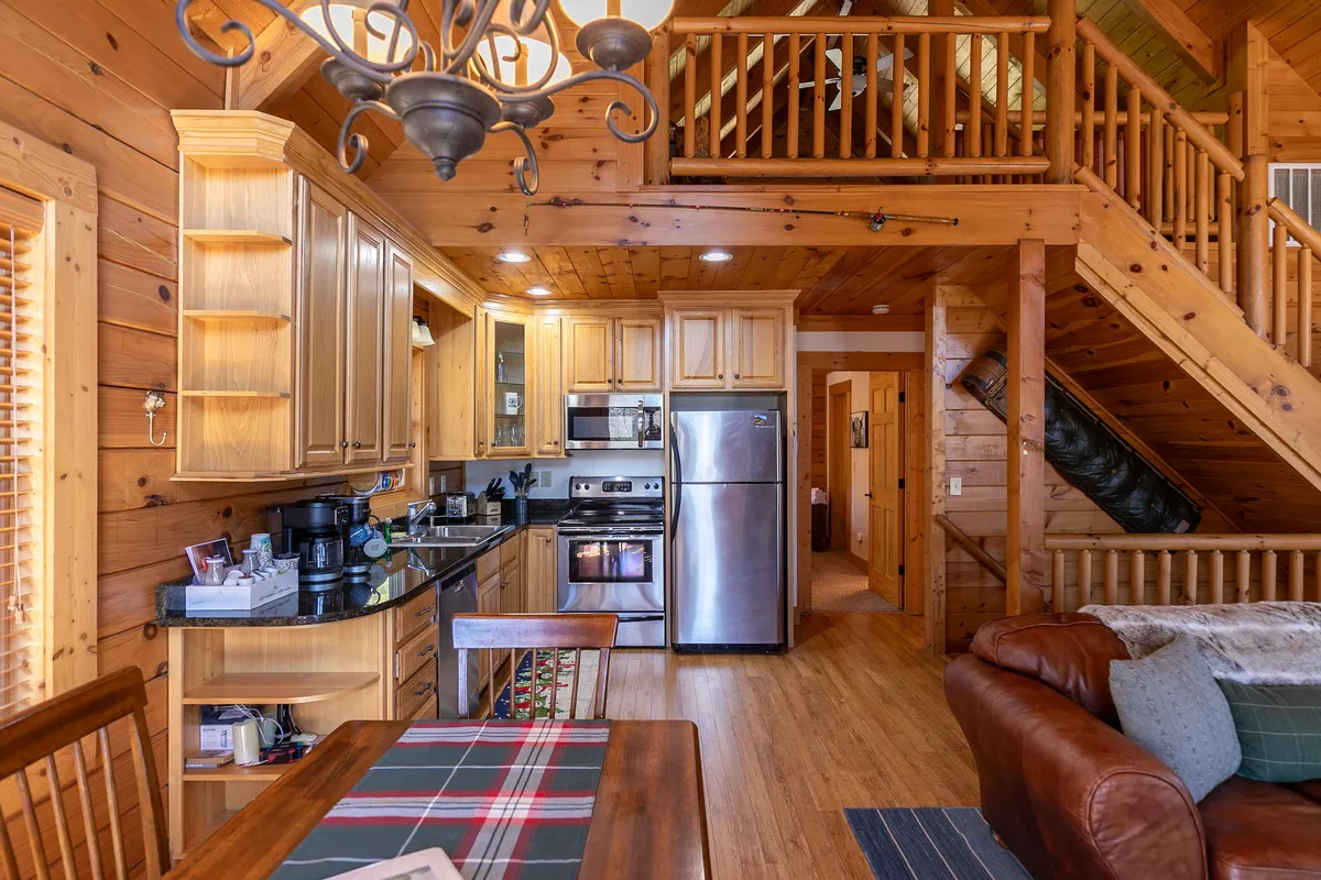 An open concept kitchen and dining space with a visible staircase and a cozy living room couch, all bathed in natural light. The area feels inviting, perfect for family meals or group gatherings, and reflects an upgraded, welcoming environment.
