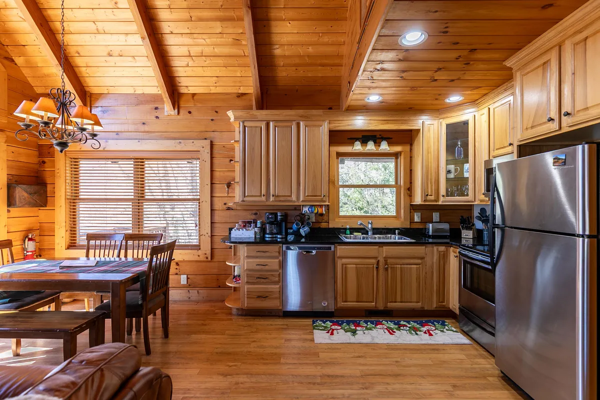 This image spotlights a bright kitchen and dining area, with a large window looking out into nature, wooden cabinetry, and a welcoming atmosphere. The scene feels open to the outdoors, ideal for post-adventure meals.