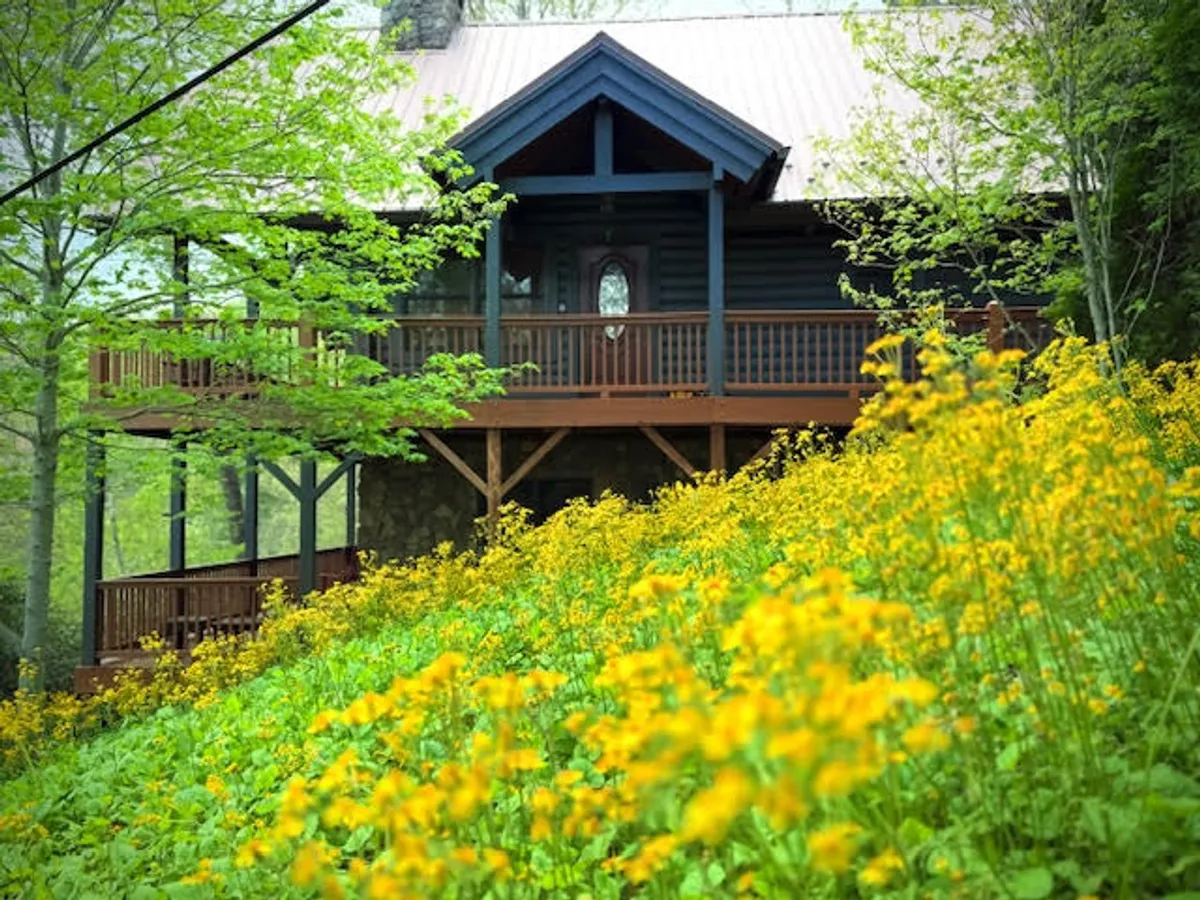 The exterior of the house with its inviting wooden deck, vibrant yellow flowers, and lush surrounding greenery. The scene suggests peaceful moments spent relaxing on the deck or enjoying the views, with plenty of space for barbecues and leisure activities.