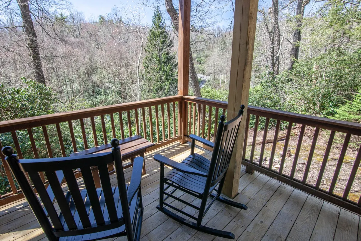 The image features classic rocking chairs lined up on a wooden deck, set against a backdrop of trees. The peaceful scene invites quiet mornings, nature-watching, and intimate conversations while enjoying the surrounding landscape.